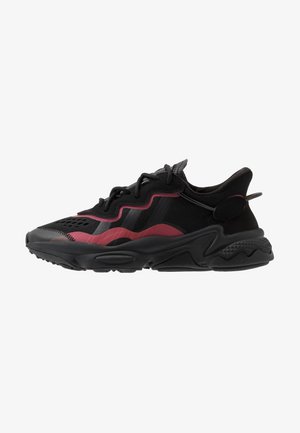Black athletic shoe with burgundy accents, featuring a mesh upper, textured sole, and distinctive wavy design elements. Light on cushioning.