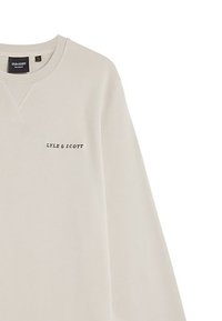 Sudadera de color beige claro con cuello redondo, detalle de costura en forma de V y logo negro "LYLE & SCOTT" en el lado izquierdo del pecho. Textura suave y diseño casual.