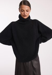 Czarny, oversize sweter z golfem, wykonany z miękkiego materiału dzianinowego, z luźnymi rękawami i swobodnym krojem, w połączeniu z ciemną skórzaną spódnicą.