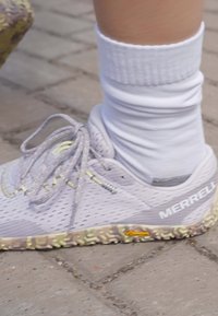 Chaussures de trail violet clair avec tige en mesh, accents jaunes et semelle texturée multicolore. Chaussettes blanches visibles en partie au niveau des chevilles.
