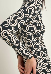 Long-sleeved garment featuring a black and cream geometric hexagonal pattern. Made of a smooth, stretchy fabric with a fitted design.