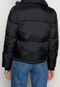 Chaqueta acolchada negra con acabado brillante, que presenta un cuello alto y puños acanalados. El diseño incluye secciones horizontales con costuras y un corte corto.