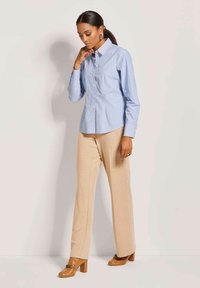 Light blue striped button-up shirt with pointed collar, paired with beige wide-leg pants and brown heeled shoes. Accessories include gold earrings.