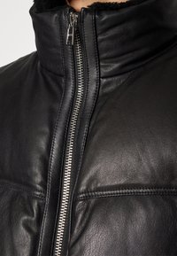 Svart läderjacka med hög krage, silverfärgad dragkedja och slät textur. Har horisontell sömnad på framsidan och mjukt foder.