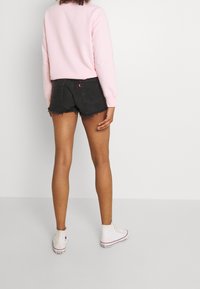 Roze sweatshirt met lange mouwen, zwarte denim shorts met rafelige zoom, en witte hoge sneakers met rode accenten.