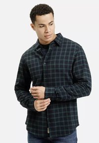 Zielono-czarna koszula flanelowa w kratkę z długimi rękawami, zapięciem na guziki i zaokrąglonym dołem. Gładka faktura z luźnym krojem.