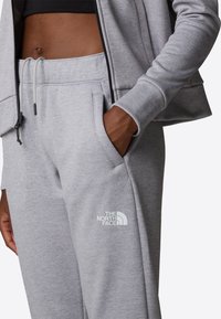 Grijze katoenen sweatpants met een trekkoord in de taille, zijzakken en een wit logo op de linker bovenbeen. Soepele textuur en casual pasvorm.