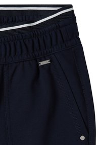 Pantalon bleu marine avec taille élastique comportant des rayures noires et blanches, poche latérale avec petite étiquette de marque argentée et détail de rivet.
