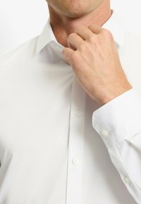 Weißes Hemd mit klassischem Kragen, Knopfverschluss und glatter Textur. Mit weißen Knöpfen an der Vorderseite und an den Manschetten ausgestattet.