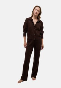 Cardigan en maille marron avec col et boutons, associé �à un pantalon marron côtelé. Les deux pièces ont une texture douce et une coupe décontractée.