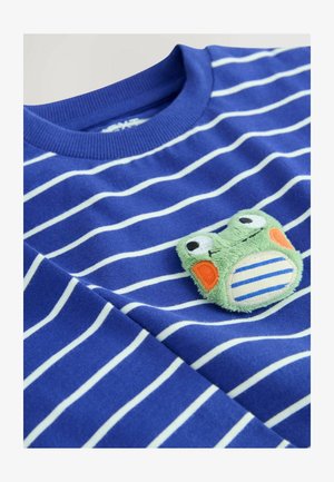 T-shirt a righe blu con strisce bianche, caratterizzata da una toppa in tessuto di rana verde testurizzata con dettagli arancioni e un design a righe sulla pancia.