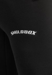 Sorte atletik leggings med en glat tekstur, med hvidt "SMILODOX"-logo trykt på den nederste del af benet. Almindelig pasform og elastisk materiale.