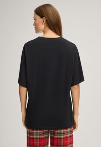 Zwart T-shirt met korte mouwen en een losse pasvorm, ronde halslijn en zachte katoenen stof, gecombineerd met rode geruite broek met een geblokt patroon.