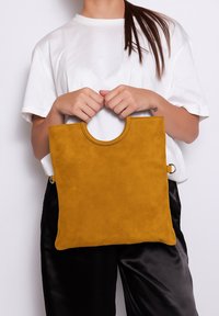 Borsa a mano gialla in suede con manico circolare e accessori laterali. La borsa ha una texture liscia e un design quadrato minimalista.