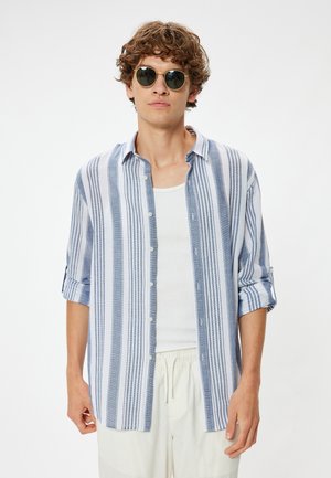 Blauw-wit gestreepte button-upshirt van lichtgewicht stof, met opgerolde mouwen en een relaxte pasvorm. Gecombineerd met ronde zonnebrillen.