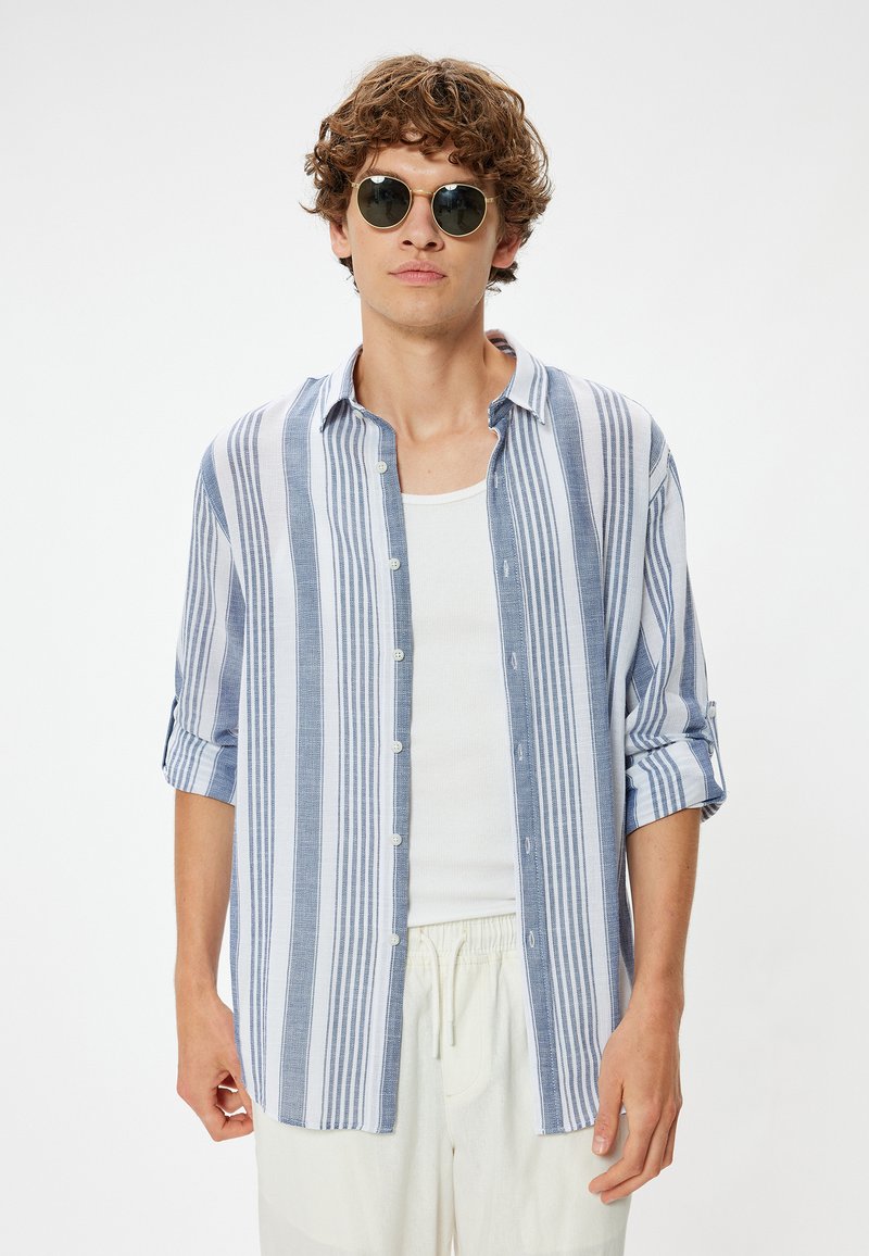 Blauw-wit gestreepte button-upshirt van lichtgewicht stof, met opgerolde mouwen en een relaxte pasvorm. Gecombineerd met ronde zonnebrillen.