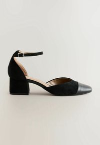 Chaussure à talon noire avec tige en daim, bout pointu et embout en cuir. Comprend une bride de cheville ajustable et un talon bloc épais.