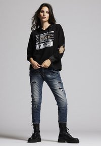 Black hooded sweatshirt with graphic print, alongside blue distressed jeans. Black lace-up combat boots complete the outfit.