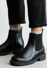 Botas Chelsea de cuero negro con paneles laterales elásticos, punta redonda y un tacón bajo tipo bloque. Suela texturizada y tirador para facilitar su uso.