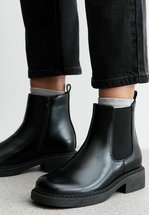 Botas Chelsea de cuero negro con paneles laterales elásticos, punta redonda y un tacón bajo tipo bloque. Suela texturizada y tirador para facilitar su uso.