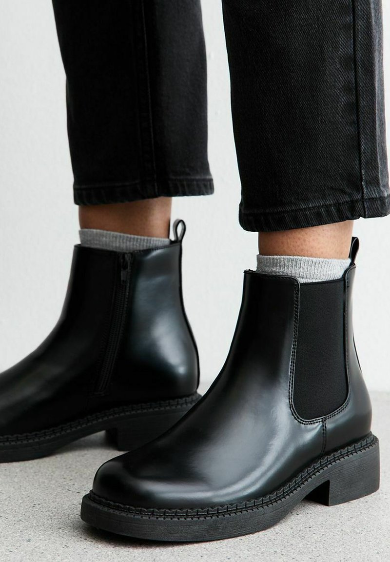 Botas Chelsea de cuero negro con paneles laterales elásticos, punta redonda y un tacón bajo tipo bloque. Suela texturizada y tirador para facilitar su uso.