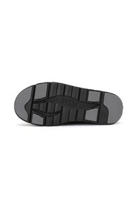 Semelle de chaussure noire avec un design à motifs, en matériau caoutchouteux, et surface texturée avec des zones d'accent gris pour une meilleure adhérence.