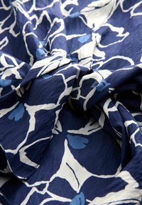 Mörkblått tyg med ett vitt och ljusblått blommönster, med en texturerad yta och mjukt fall. Tvinnad och lager-på-lager textil.