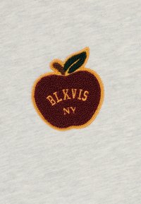 Logo de manzana bordado en color burdeos con texto amarillo "BLKVIS NV" sobre un fondo de tela gris claro, con una hoja verde y un tallo marrón.