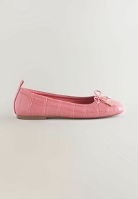 Une ballerine plate rose avec texture crocodile, talon bas, bout rond, petit nœud avec embouts dorés sur un fond clair.