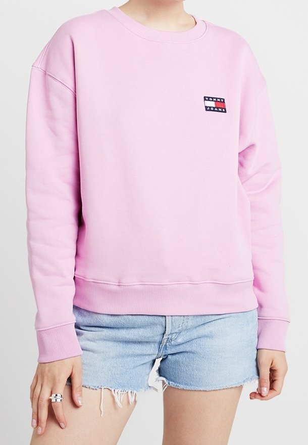 Rosa sweatshirt med rund halsringning, ribbade ärmslut och nederkant. Har en liten Tommy Jeans-logotyp på vänster bröst. Bärs med jeansshorts.