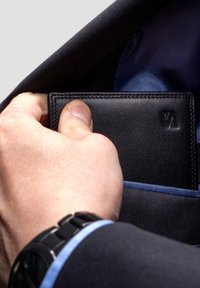 Black leather wallet with embossed logo, held by a hand, partially inserted into a blue-lined suit pocket. Smooth texture and sleek design.