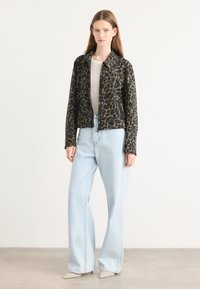 Zwarte en groene luipaardprint jack met ritssluiting, cropped ontwerp met een kraaghalslijn, gecombineerd met lichtblauwe wijde jeans.