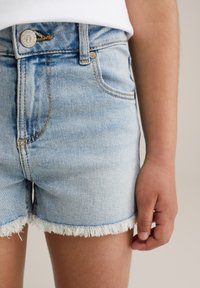 Hellblaue Jeansshorts mit ausgefranstem Saum, ausgestattet mit gelben Nähten und einem Knopfverschluss. Taschen sind vorne und hinten sichtbar.