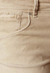 Beige kordväv med vertikala ribbor, med en liten framficka och en metallknappdetalj vid midjan.