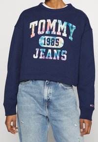 Marinblå croppad sweatshirt med "TOMMY JEANS"-logotyp i flerfärgad gradient, med ribbade ärmslut och en vit lagerkrage under.