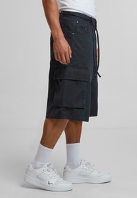 Cargo shorts in dark blue cotton, featuring multiple pockets, a drawstring waist, and a relaxed fit, paired with white sneakers and socks.