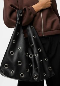 Zwarte leren tas met een slonzig ontwerp en zilveren oogjes als versiering. Zachte textuur met grote openingen voor een casual uitstraling.