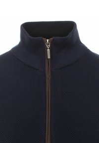 Marineblauer Reißverschluss-Pullover mit hohem Kragen, aus strukturiertem Material und einem kontrastierenden braunen Reißverschluss. Glatte Oberfläche am inneren Kragen.