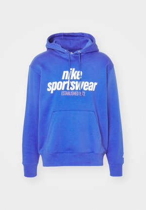 Royalny niebieski hoodie z kieszenią typu kangur, kapturem ze sznurkiem oraz białym logo "nike sportswear ESTABLISHED 1972" z przodu. Materiał bawełniany.