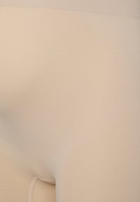 Gros plan d’un tissu beige sans couture avec des coutures visibles et une texture subtile, suggérant un ajustement serré sur une surface courbée.