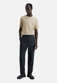 Beige katoenen t-shirt met korte mouwen, gecombineerd met donkergrijze linnen broek. De outfit wordt aangevuld met donkere instappers.