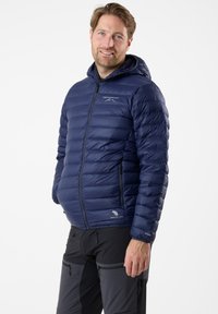 Marineblaue Steppjacke mit Kapuze, ausgestattet mit einem Reißverschluss, gesteppter Textur, Daunen-Isolierung und Branding auf der Brust.