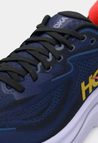 Ναυτικό μπλε παπούτσι για τρέξιμο με άνω μέρος από διαπνέον πλέγμα, μαύρο σύστημα κορδονιών, κίτρινο λογότυπο και επενδυμένη λευκή μεσαία σόλα με υφή.