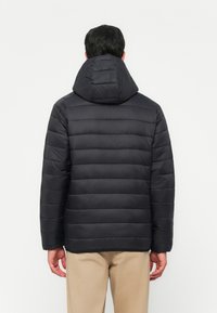 Puffjacke in dunkelblau mit horizontaler Steppung, abnehmbarer Kapuze und elastischen Bündchen. Glattes Gewebe mit weicher Textur.