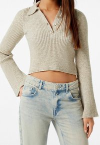 Beige ribbad långärmad topp med krage och tre knappslå, i kombination med ljusblå, lätt slitna högmidjade jeans.