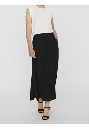 Femme portant un haut blanc sans manches et une longue jupe noire fendue sur le côté, assortis à des talons ouverts noirs à bride cheville.