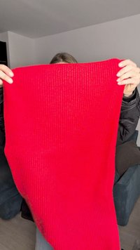 Red knit blanket held up, featuring a textured ribbed pattern. Material appears warm and thick, suitable for cozy use.