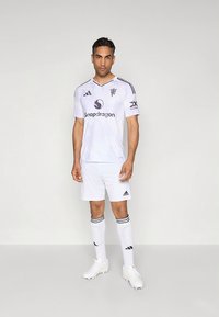 Camisola de futebol branca com detalhes roxos, apresentando um decote em V, logotipos de patrocinadores e riscas diagonais. Combinada com calções brancos, meias com riscas pretas e chuteiras.