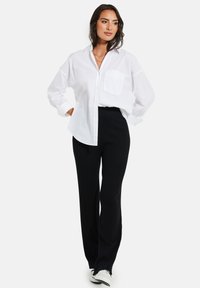 Witte button-up shirt met een borstzak, gecombineerd met zwarte geribbelde flare pants en witte sneakers. De outfit heeft een comfortabele pasvorm.