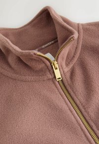 Fleece-Zip-Jacke in sanftem, staubigem Rosa. Mit einem goldenen Reißverschluss und einem Stehkragen. Die Textur ist flauschig und weich.